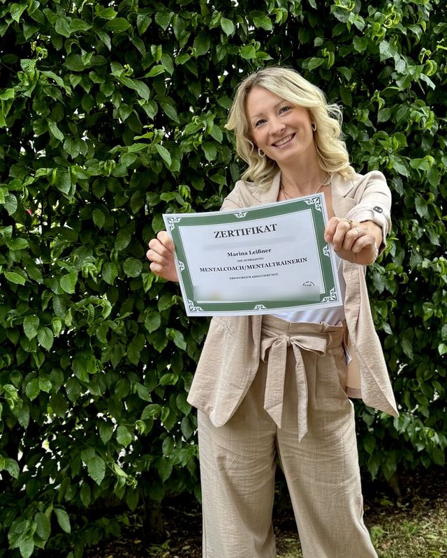 Marina hält lächelnd ihr Zertifikat als Mentalcoach und Mentaltrainerin